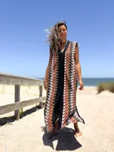 Vestido largo tejido con patrón geométrico en tonos marrón, beige, blanco y negro. Tiene escote en V y corte holgado.