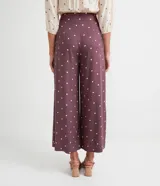 Pantalón pantacourt de viscosa color lila con estampado de pequeños cuadrados blancos. Tiene pinzas delanteras, bolsillos laterales y cierre con botones.