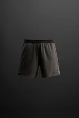 Shorts deportivos color gris oscuro confeccionados en tejido técnico ligero y elástico con forro interior, cintura elástica ajustable con cordón, bolsillos laterales, bolsillo de seguridad en espalda con cierre de cremallera, bajo con aberturas laterales y detalle de logo estampado en pernera.