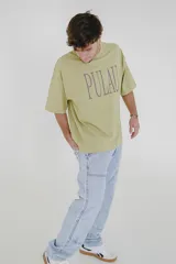 Remera verde con estampado de la palabra "Pulau" en color lila.