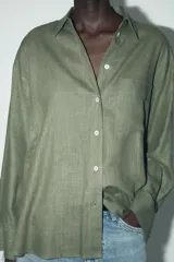 Camisa amplia color negro confeccionada con hilatura de lino. Tiene cuello solapa, manga larga, bolsillo de plastrón en el delantero, bajo asimétrico y cierre frontal con botones.