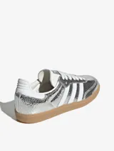 Zapatillas Adidas Samba OG W plateadas metalizadas con efecto craquelado, las tres tiras laterales blancas y suela de goma color caramelo.