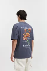 Remera color crudo de corte amplio, con mangas cortas y estampado en la espalda con flores rojas y texto en negro.