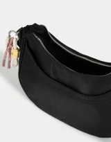 Bandolera hobo negra de tela deportiva con correa regulable, cierre superior, bolsillo frontal y charm lateral decorativo.