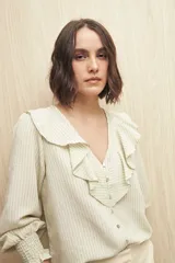 Camisa blanca a rayas verticales, con escote en V, mangas 3/4 con puños elastizados y volados.