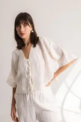 Blusa color crema confeccionada en lino, con mangas cortas, escote en V y lazos frontales.