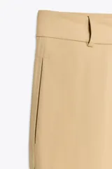 Pantalón color beige de tiro alto con bolsillos delanteros y falsos bolsillos de vivo en la espalda, de pierna ancha y corte recto. Cierre frontal con cremallera y botón.