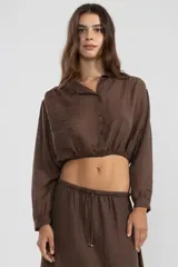 Blusa corta color marrón chocolate en tejido arrugado liviano, con cuello mao, botones al frente y mangas abullonadas terminadas con ruedo elastizado.