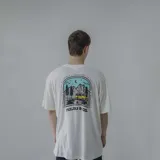 Remera color crema con estampa en la espalda de una combi amarilla en un paisaje de montaña.