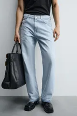 Pantalón de jean celeste de corte flare, con tiro medio, cinco bolsillos, cierre frontal con cremallera y botón, y bajo con acabado irregular.