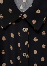 Vestido midi camisero negro con estampado de lunares color beige, cierre frontal con botones, lazo en la cintura y mangas largas con puños abotonados.