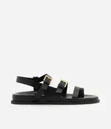 Sandalias negras con tiras de cuero sintético, suela plana y hebillas doradas.