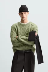 Sweater verde claro de punto con cuello redondo y mangas largas. Presenta diseño de trenzas en el centro y en las mangas.