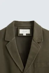 Blazer color verde militar de algodón con efecto lavado, corte relaxed fit, cuello con solapas de muesca, manga larga, bolsillos frontales de plastrón y cierre frontal con botonadura.