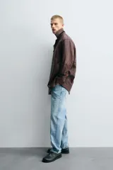 Cazadora de hombre de corte relajado, confeccionada en piel con textura irregular color marrón oscuro (vino/borgoña). Presenta cuello solapa, manga larga con puño abotonado, bolsillos de vivo en cadera, bolsillo interior y cierre frontal con botonadura.