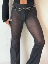 Calza negra de tela traslúcida con brillos, corte acampanado y cintura alta con cinturón de cuero negro con apliques metálicos.