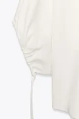 Blusa blanca de lyocell con cuello redondo, manga corta abullonada ajustable con cordones, bajo redondeado y cierre en la espalda con abertura y botón.