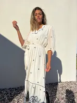 Vestido largo blanco con bordados azules, escote en V, mangas 3/4 abullonadas y lazo en la cintura.