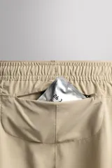 Pantalón corto deportivo color marrón oliva, con cintura elástica ajustable con cordón, bolsillos frontales y bolsillo trasero con cierre. Presenta forro interior y detalle de logo estampado en la pernera.
