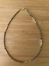 Collar corto de cuentas facetadas color gris oscuro, con detalles de cuentas cúbicas doradas y cadena de alargue dorada.