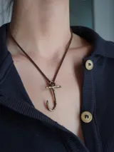 Gargantilla marrón de cuero con dije de bronce en forma de letra M.