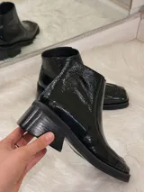 Bota de charol negra con punta cuadrada, tacón grueso y cierre lateral.