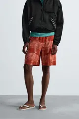 Short de baño color ladrillo con estampado de líneas curvas en color salmón. Tiene cintura elástica ajustable con cordón, bolsillos laterales y trasero.