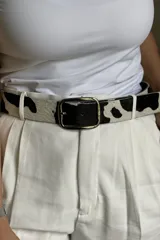 Cinturón con estampado animal print de vaca, hebilla metálica plateada y dos remaches plateados.