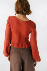 Blusa blanca de lino con escote en V, mangas largas abullonadas y frunce central.