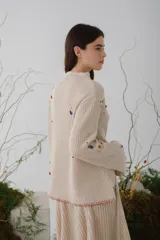 Sweater beige de lana con cuello redondo y mangas largas. Presenta detalles de bichos tejidos a contratono en la parte superior delantera.