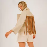 Chaqueta corta color beige de cuero, con cuello clásico, cierre frontal con botones y flecos de cuero marrón en la parte superior de la espalda.