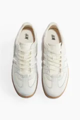 Championes deportivos color crema con detalles en gris y suela marrón. Presentan collarín acolchado, cordones y logo bordado en el lateral. Grosor de la suela 2,5 cm.