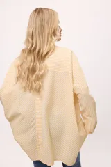 Camisa oversize a rayas verticales color amarillo y blanco, con cuello camisero, manga larga y cierre frontal con botones.