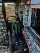 Remera verde oscuro de corte boxy/oversize con logo "M" bordado en dorado en la parte superior de la espalda.