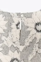 Top sin mangas con estampado de flores blancas y negras, cuello redondo, corte peplum y cierre con botón en la espalda.