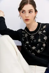 Buzo negro de algodón con cuello redondo y mangas largas. Presenta apliques bordados de piedras brillantes en forma de flores y otros motivos decorativos en el frente.