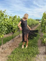 Vestido corto tejido en lurex negro con detalles en blanco, de corte holgado, mangas cortas y flecos en el ruedo.