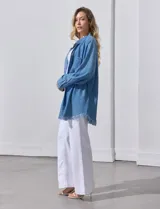Camisa de jean celeste, marca Hester & Orchand, de corte oversize con cuello con solapa, escote en V y abertura central con botones. Delantera con bolsillos aplicados, mangas largas regulables con presilla y botón, y ruedo desflecado.