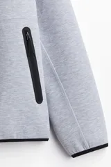 Campera deportiva gris con capucha, cierre frontal y bolsillos laterales con cierre. Confeccionada en tejido funcional DryMove™ que ayuda a absorber el sudor.