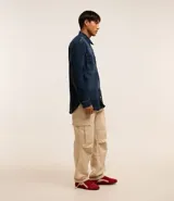 Camisa masculina oversized confeccionada en jeans azul oscuro, con cuello inglés, manga larga, puño ajustado, abotonado delantero y dos bolsillos cargo en el pecho.