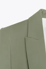 Blazer color blanco, abierta, con cuello solapa y hombreras. Manga tres cuartos acabada en vuelta con trabilla y botón dorado. Bolsillos delanteros con solapa.