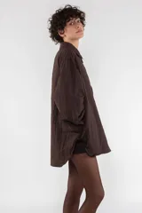 Camisa blanca oversize de nailon arrugado, con cuello clásico, cierre frontal con botones, manga larga raglán, puños abotonados, bolsillo utilitario en el pecho, bolsillos laterales y canesú abotonado en la espalda.