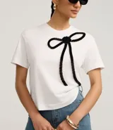 Remera blanca de algodón con cuello redondo, mangas cortas y bordado de lazo negro en la parte delantera.