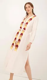 Saco color crema con bordado de flechas en tonos amarillo, marrón y rojo. Tiene mangas largas con detalle de puntilla y cinturón fino del mismo tejido.
