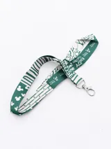 Llavero con cinta estampada con motivos de Mickey Mouse y la frase "Enjoy the now" en verde y blanco. Incluye gancho metálico plateado.