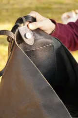 Bolso maxi negro de cuero con flecos y botón de guampa. Tiene bolsillo interior y cierre metálico.