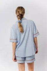 Pijama de algodón color blanco, compuesto por una camisa de manga corta abotonada con cuello solapa y un bolsillo en el pecho, y un short con elástico en la cintura. Ambas prendas tienen un detalle de picot marrón en los bordes.