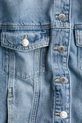 Campera trucker corta de denim celeste, con cuello clásico, cierre frontal con botones metálicos, mangas largas con puños abotonados, bolsillos superiores con solapa y botón, bolsillos laterales y trabillas ajustables con botones en los laterales del bajo.