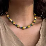 Collar corto con cuentas de diferentes colores y formas: esferas doradas con detalles en rojo, cuentas facetadas color verde esmeralda y cuentas pequeñas color rosa y rojo.