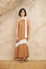 Vestido largo color marrón con corte debajo del busto y falda acampanada. Presenta cuello halter con lazo blanco.